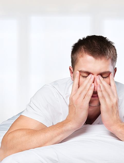 Tired man lying on stomach in bed rubbing his eyes