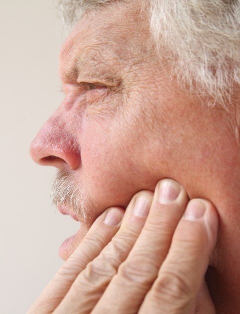 Man with jaw pain holding his cheek