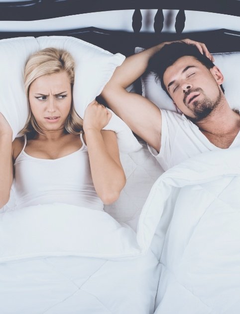 Woman frustrated in bed next to snoring man in need of oral appliance therapy for sleep apnea
