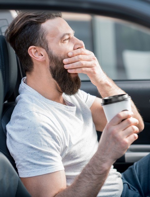 Tired man drinking coffee and yawning while driving before oral appliance therapy for sleep apnea