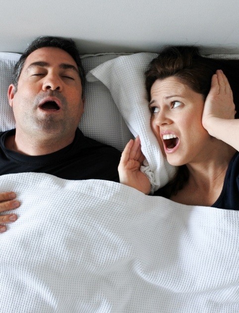Woman frustrated in bed next to a snoring man