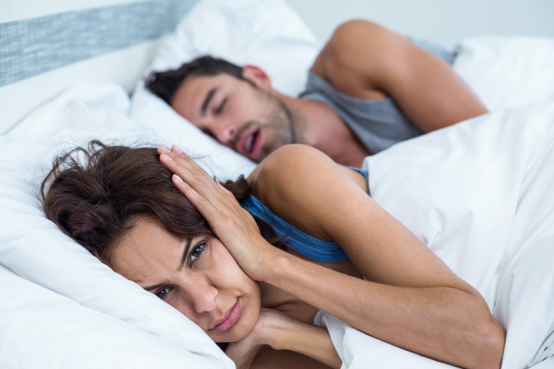 Annoyed woman covering her ears as man snores nearby