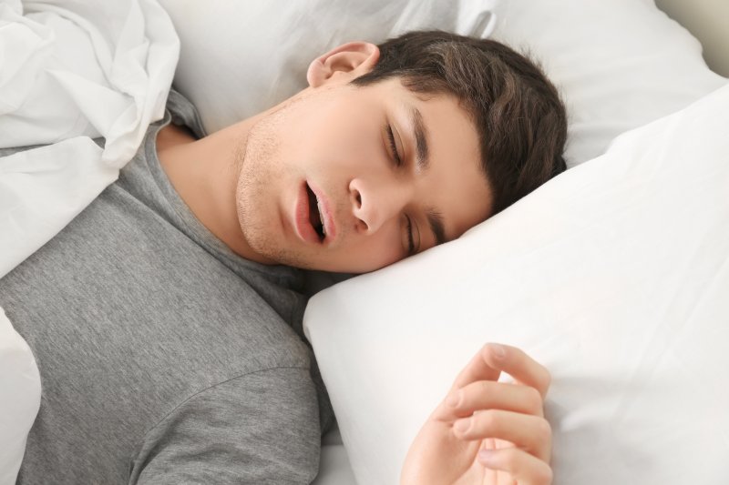 Young man in grey shirt snoring in bed