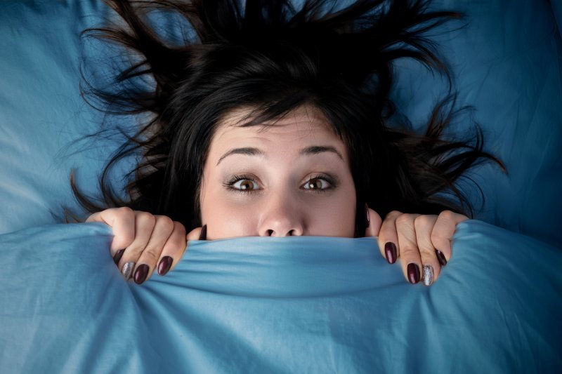 Woman hiding under blankets after waking up from nightmare