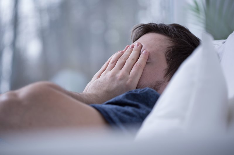 Man lying awake in bed covering his face