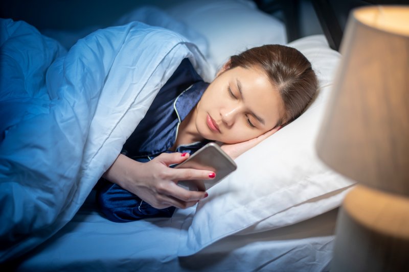woman looking at phone while in bed in Topeka