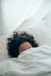 Woman in bed with blanket over face