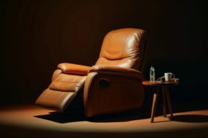 Brown recliner chair in a dark room with a small side table with water and a mug.