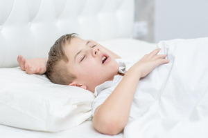 Little boy snoring in bed with white sheets